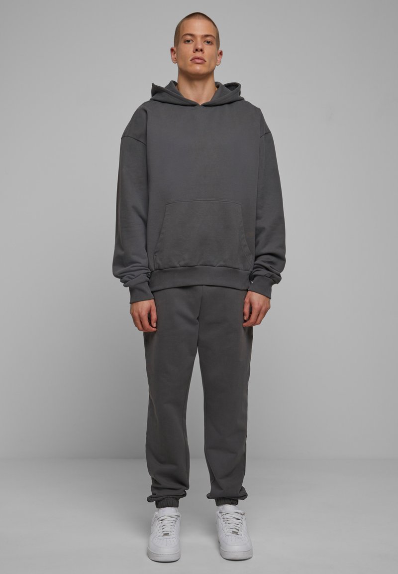 Felpa grigia con cappuccio e pantaloni della tuta abbinati realizzati in tessuto morbido, con tasca frontale, polsini a costine e sneakers bianche.