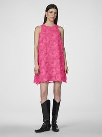 Kort rosa klänning med en texturerad fransdesign, ärmlös stil och en lös passform. Buren med svarta knähöga stövlar.