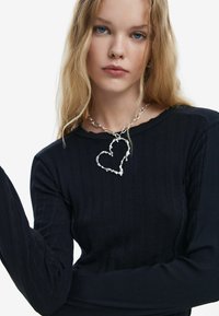 Fekete bordázott hosszú ujjú felső, kerek nyakkivágással, díszes ezüstlánccal, szív alakú medállal.