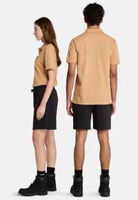 Due persone indossano abiti casual: una polo color beige e pantaloni corti neri. La donna ha una vestibilità leggermente aderente, mentre la camicia dell'uomo è regolare. Entrambi indossano stivali neri.