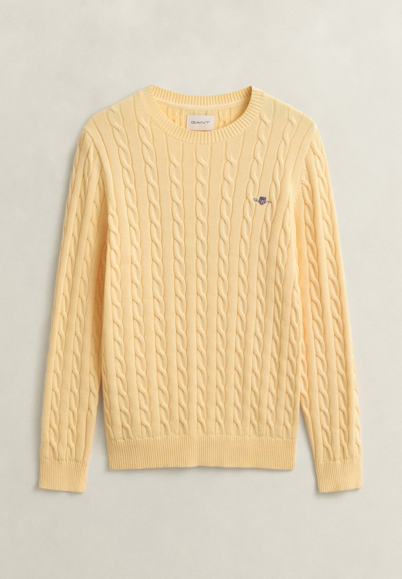Pull jaune clair en maille torsadée avec manches longues, poignets et ourlet côtelés, col rond, et petit logo brodé sur la poitrine.