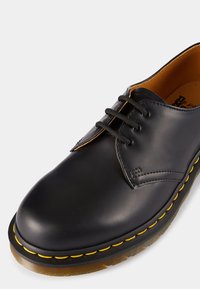 Shoe preto de couro com atacadores, com ponta arredondada, costura amarela e sola texturizada. Inclui seis ilhós e um acabamento suave.