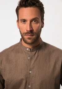 Camicia in lino marrone con colletto alla coreana, chiusura frontale con bottoni e una texture sottile, caratterizzata da cuciture visibili e un design aderente.