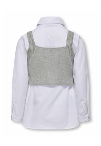 Grå strikket crop top med brede stropper over en hvid skjorte med knapper. Toppen har en ribbet tekstur og en flat kant.