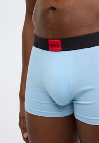 Ανοιχτό μπλε βαμβακερά μποξεράκια με μαύρη ζώνη μέσης που φέρει κόκκινη ετικέτα με το λογότυπο «HUGO». Σχέδιο χωρίς ραφές με εφαρμοστή γραμμή.