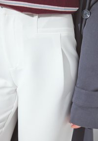 Białe spodni o dopasowanym kroju z gładkiego materiału, z bocznymi kieszeniami i elegancką sylwetką, zestawione z ciemnoszarym płaszczem na guziki.