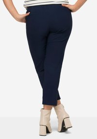 Marineblaue knöchellange Hose mit glatter Textur, ausgestattet mit einer Gesäßtasche und kombiniert mit off-white Blockabsatz-Ankle Boots.