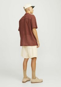 Camisa marrón de manga corta y semitransparente con un diseño estampado; combinada con pantalones cortos de pana color crema y zapatos beige.