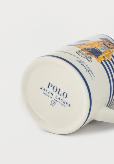 Fehér porcelán bögre kék csíkokkal, amelyen egy sárga dzsekis és kék rövidnadrágos medve látható, "Polo Ralph Lauren" logóval és az alján "Made in China" felirattal.