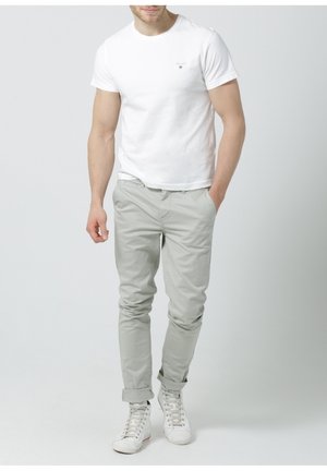 Witte katoenen t-shirt met een klein logo, gecombineerd met lichtgrijze chinos en witte high-top sneakers. Eenvoudige, casual pasvorm met opgerolde mouwen.