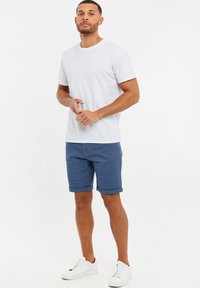 Hvid kortærmet t-shirt parret med blå denimshorts, opsmøgede ærmer, fuldendt med hvide sneakers. Simpelt, afslappet design.