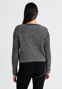 Stickad tröja i svart och vitt med ett strukturerat mönster, rundad halsringning och långa ärmar. Kort modell med ett ribbat nederkant.