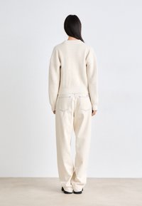 Pull côtelé crème avec épaules tombantes, associé à un pantalon ample crème avec poches arrière et surpiqûres contrastantes.