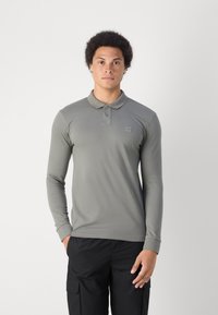 Polo shirt met lange mouwen in olijfgroen, gemaakt van een gladde stof. Heeft een kraag, twee knopen en een kleine logopatch op de borst.
