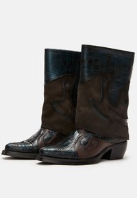 Western-style boots featuring glossy dark blue crocodile-textured leather and brown suede accents with blue stitching and curved designs.