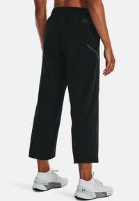 Black athletic pants with a relaxed fit, featuring an elastic waistband, side pockets, and reflective accents on the thighs.