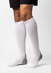 Calze a compressione bianche con un design testurizzato, caratterizzate da dettagli grigi e aree rinforzate. Le calze si estendono sopra i polpacci.