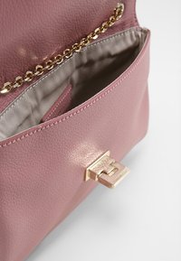 Różowa skórzana torebka o fakturowanej powierzchni, ze złotym łańcuszkiem jako paskiem oraz metaliczną klamrą. Wnętrze wyściełane jest gładką tkaniną.