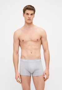 Graue trunkförmige Unterwäsche mit einem weichen, elastischen Bund, der den Markennamen "HUGO" in Weiß trägt. Glatte Textur und figurbetontes Design.