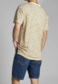 Camiseta de manga corta de color beige con textura y escote redondo, combinada con pantalones cortos de mezclilla azul con bolsillos traseros y corte recto.