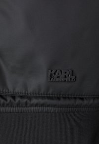Čierny nylonový materiál má štruktúrovaný vzor s výrazným matným čiernym logom "KARL LAGERFELD" našitým na spodnej časti.