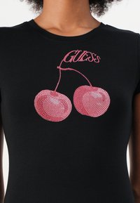 T-shirt nera aderente con una grafica di ciliegie in strass rosa e la parola "GUESS" sopra in strass abbinati. Maniche corte.