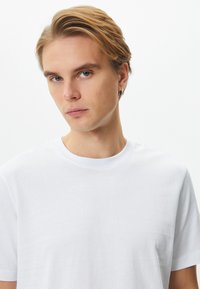 Valkoinen puuvillapaita, jossa on pyöreä kaula-aukko ja lyhyet hihat, esittelee sileää tekstuuria ja yksinkertaista muotoilua. Ei kuvioita tai koristeita.