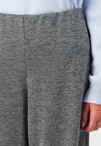 Nærbilde av grått houndstooth-mønstret bukser sammen med en lys blå langermet skjorte, som viser en avslappet passform og synlig hånd.
