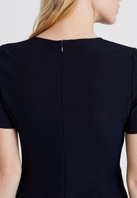 Vestido de color navy con un tejido suave, mangas cortas y cierre de cremallera en la parte posterior. Diseño sencillo con una silueta ajustada.