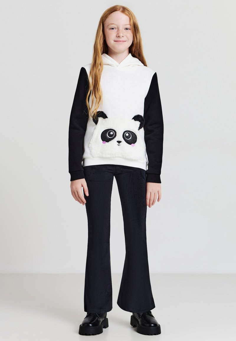 Felpa bianca e nera con design di panda sulla tasca, abbinata a pantaloni neri svasati e scarpe nere chunky. Tessuto morbido, stile casual.