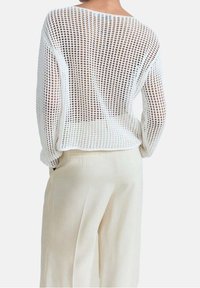Pull en laine blanc, ample et court, présentant un motif de tricot ouvert. Associé à un pantalon clair à jambes larges pour le contraste.