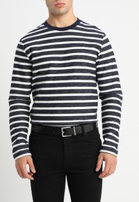 Maglietta a maniche lunghe a righe navy e bianche con collo a giro, realizzata in tessuto testurizzato, abbinata a pantaloni neri e una cintura nera.