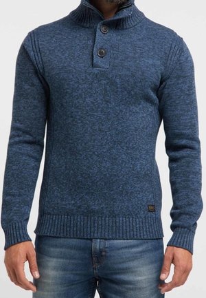 Blauer Strickpullover mit hohem Kragen, zwei-Knopf-Leiste, gerippten Bündchen und Saum sowie einem strukturierten Muster. Über Denim getragen.