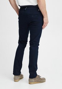 Mørkeblå bukser vist bagfra, med slim fit, glat stof, to baglommer og diskrete sømdetaljer.