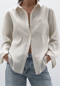 Lyscreme knap-op skjorte med spids krave og en enkelt brystlomme, parret med blå højtaljede jeans med afslappet pasform og blød tekstur.