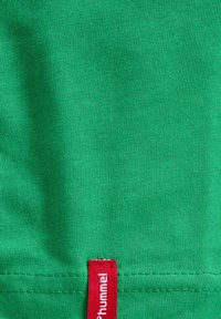 Grøn bomulds T-shirt med ribbet tekstur og et rødt mærke med brandnavnet "Hummel" ved kanten.