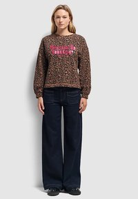 Leopard print sweatshirt with pink text "french muse," paired with dark wide-leg jeans. The outfit features long sleeves and a relaxed fit.