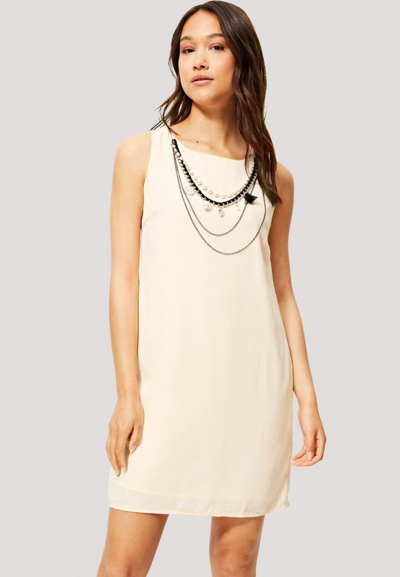 Vestido sin mangas de color crema hecho de una tela ligera, con collares de cuentas en capas en blanco y negro como acentos. Textura suave y forma clásica.