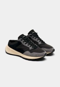 Baskets grises et noires en mélange de suède et tissu, avec des lacets ronds, une semelle amortissante et une semelle intermédiaire beige. Logo sur la languette.