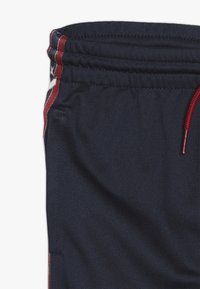 Marineblauwe sportshorts met een elastische tailleband, rode trekkoord en contrasterende zijpanelen in rood en wit met een sterrenpatroon.