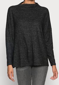 Svart, långärmad topp i texturerad tyg med vida axelband. Har en lös passform och en ojämn nederkant. Bärs tillsammans med grå jeans.