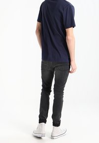 Camiseta de algodón azul marino, jeans gris ajustados y zapatillas altas blancas. Costuras visibles y diseño de pierna ajustada en los pantalones.