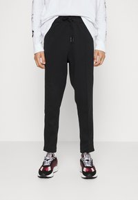 Černé zúžené jogger kalhoty vyrobené z bavlněné směsi s elastickým pasem a šňůrkou. Spárováno s bordó a černými sportovními botami.