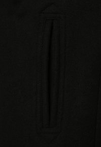 Tessuto di lana nera con un dettaglio a fenditura verticale. La texture appare morbida e liscia con un design pulito e minimalista.