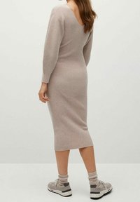 Robe tricotée à côtes couleur beige clair avec un dos en V et des manches longues, assortie à des baskets grises et des chaussettes de cheville assorties.