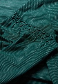 Türkisfarbener Stoff mit dünnen weißen Streifen, der eine geraffte Nahtdetails aufweist. Glatte Textur mit einem leichten Glanz. Geometrisches Muster an der Naht.