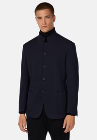 Chaqueta azul marino con cuello mao, cierre de botones, dos bolsillos frontales y una textura de tela suave. Diseño ajustado.