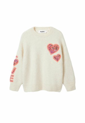 Pull en maille crème avec deux patchs en forme de cœur rose sur la poitrine et texte brodé rose sur la manche gauche.
