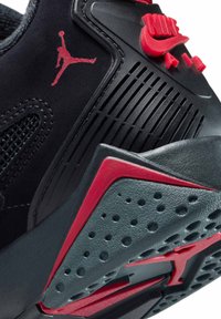 Baskets noires avec des accents rouges, présentant un dessus texturé, des panneaux en maille et une semelle en caoutchouc avec un logo proéminent et des ventilations.