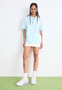 Light blue cotton t-shirt with short sleeves, paired with a pale skirt. Worn with white and lavender athletic shoes and white socks.